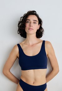 Laikaputra ribbed bralette mėlynai su plačiomis petnešomis, turinti apvalų kaklą ir be siūlių dizainą. Lygus paviršius su derančiomis aukštomis kelnaitėmis.