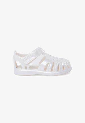 Sandalia de gelatina translúcida blanca con puntera cerrada, correa ajustable de velcro y laterales y parte superior ventilados.