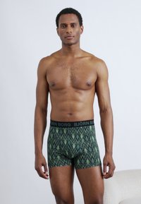Moške boksarske spodnje hlače z zelenim cikcak vzorcem in črnim pasom z napisom "BJÖRN BORG." Material deluje raztegljiv in mehak.