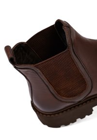Bruine leren enkellaars met elastische zijpanelen, textuur binnenin, ribbelaccenten en een robuuste zool met grip.