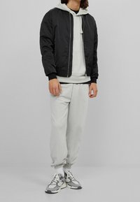 Svart bomberjacka över en ljusgrå hoodie, parat med ljusgrå joggingbyxor. Grå och vita sneakers fulländar outfiten. Släta tygtexturer.