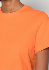 Kortærmet orange bomulds T-shirt med rund hals; glat tekstur med en afslappet pasform og minimale syninger på ærmerne.