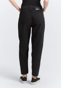 Jeans de mezclilla negra con cintura alta, piernas ajustadas y dos bolsillos traseros. El material tiene una textura y cuenta con una etiqueta de la marca en la cinturilla.