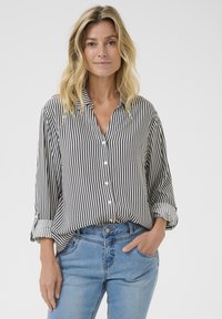 Camicia a righe bianca e nera con colletto, maniche arrotolate e vestibilità ampia. Abbinata a jeans azzurri chiari.