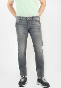 Grå denimjeans med slim fit, med en urtvättad textur, fem fickor och metallknappstängning. Bärs med svarta sneakers.