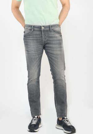 Jeans de mezclilla gris de corte ajustado, con una textura descolorida, cinco bolsillos y cierre de botón de metal. Llevados con zapatillas negras.