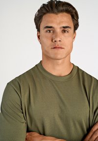 Olivgrön kortärmad t-shirt med rund halsringning. Tillverkad av mjukt tyg med en avslappnad passform. Synliga sömmar längs kragen och ärmarna.