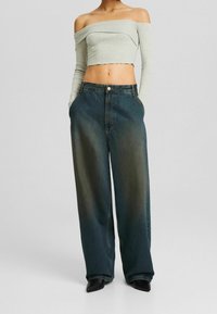 Jasnoszara, opadająca sweter w stylu cropped z prążkowaną fakturą, w zestawieniu z szerokimi dżinsami w ciemnym odcieniu, które mają kieszenie z przodu oraz zapięcie na guzik.