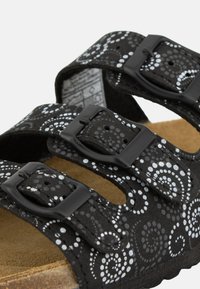 Black sandals with three adjustable straps, featuring a swirl pattern in white. Made of soft material with a cork footbed for comfort.