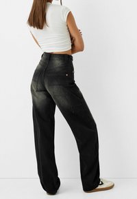 Czarne dżinsowe spodnie cargo z szerokimi nogawkami, z efektem sprania i wieloma kieszeniami. Połączone z dopasowaną białą bluzką i casualowymi trampkami.