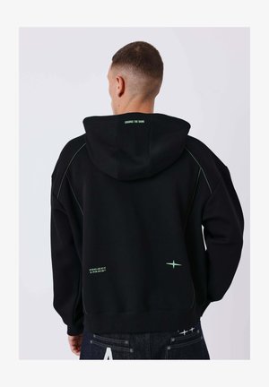 Homme vu de dos portant un sweat à capuche noir avec le texte « CHANGE THE GAME » sur la capuche et « PROJECT X PARIS » près du bas, associé à un jean sombre.