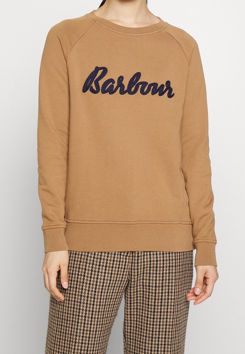 Brown sweatshirt with navy "Barbour" embroidery, raglan sleeves, ribbed cuffs, and hem. Worn over patterned trousers; smooth fabric texture.