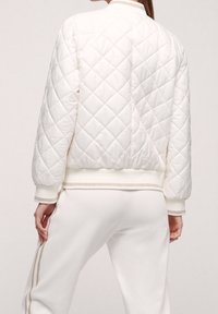 Quilted white bomber jacket with ribbed cuffs and hem, featuring metallic trim along the edges, designed for a relaxed fit.
