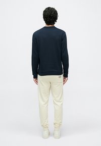 Temno modra majica z dolgimi rokavi, rebrastimi zapestji in robom; kombinirana s kremnimi jogger hlačami z majhnim logotipom na zadnjem žepu.