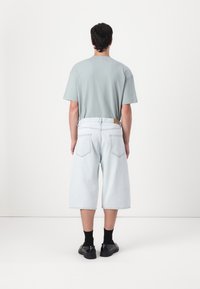 Svijetloplana oversized majica, u kombinaciji s hlačama do koljena od svijetloplavog trapera. Crne čarape i cipele upotpunjuju odijelo. Minimalni dizajnerski elementi.