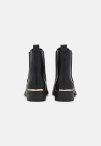 Botas de tobillo de cuero negro con paneles laterales elásticos, que cuentan con un acento dorado en el tacón y una suela de goma texturizada.