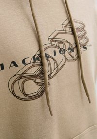 Beżowa bluza z kapturem z napisem "Jack & Jones" na tle graficznych 3D ogniw łańcucha oraz dwoma zwisającymi sznurkami.