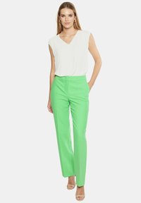 Biała, bezrękawnikowa bluzka w serek w połączeniu z jaskrawozielonymi, dopasowanymi spodniami. Materiał wydaje się lekki o gładkiej fakturze.