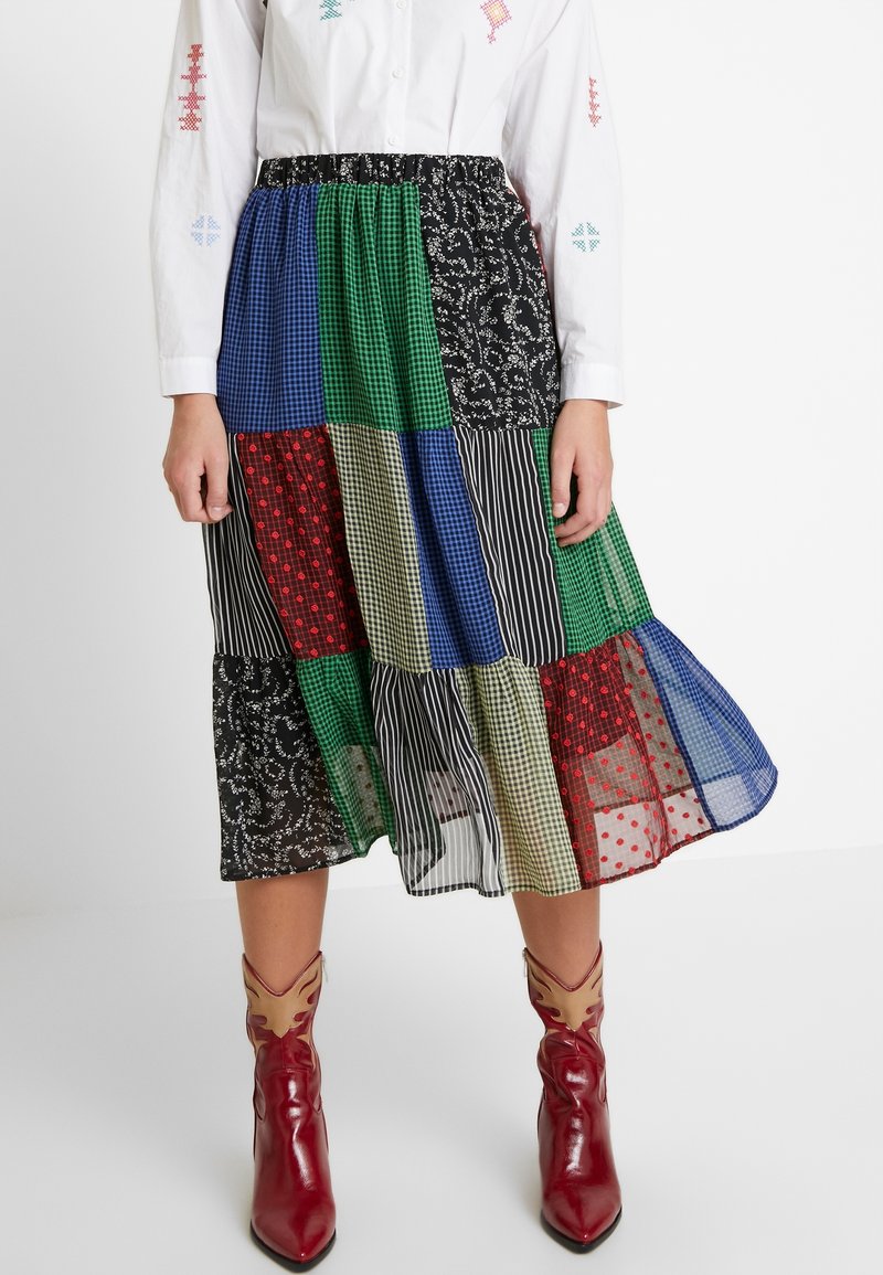 Jupe en patchwork multicolore avec des motifs floraux, à carreaux et rayés, dotée d'un ourlet en volants et d'une taille élastique. Associée à des bottines rouges.