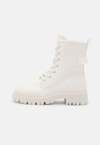 Weiße Knöchelstiefel aus glattem Material, mit einem schnürbaren Design, dickem Profilsohle und einer Zuglasche hinten für einfaches An- und Ausziehen.