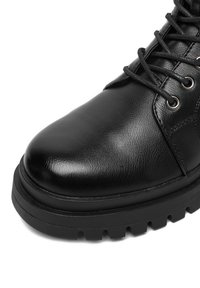 Czarne skórzane botki za kostkę o błyszczącej powierzchni, okrągłym nosku, grubej gumowej podeszwie oraz metalowymi oczkami na sznurowadła. Szczegółowe przeszycia po bokach.