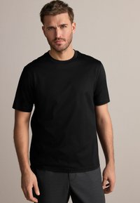 Camiseta negra de manga corta con cuello redondo, hecha de tela de algodón suave, con un ajuste clásico, combinada con pantalones grises.
