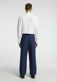 Chemise blanche à manches longues en tissu texturé, associée à un pantalon tailleur bleu marine, comportant des poches arrière et un design à jambes droites.