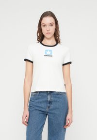 Λευκό κοντομάνικο μπλουζάκι με μαύρες μανσέτες και λαιμόκοψη. Διαθέτει μπλε λογότυπο αστέρι και το κείμενο "CONVERSE" στο κέντρο του στήθους.