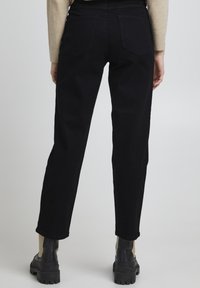 Schwarze High-Waist-Jeans mit geradem Bein, ausgestattet mit zwei Gesäßtaschen. Kombiniert mit klobigen schwarzen und beigen Stiefeln.