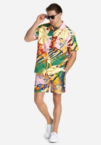 Colorful short-sleeve shirt and shorts set, featuring abstract tropical patterns in pink, yellow, green, and blue, made from lightweight fabric.