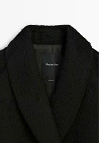 Manteau noir en tissu texturé, avec un large col et une étiquette intérieure portant le nom de la marque "Massimo Dutti."