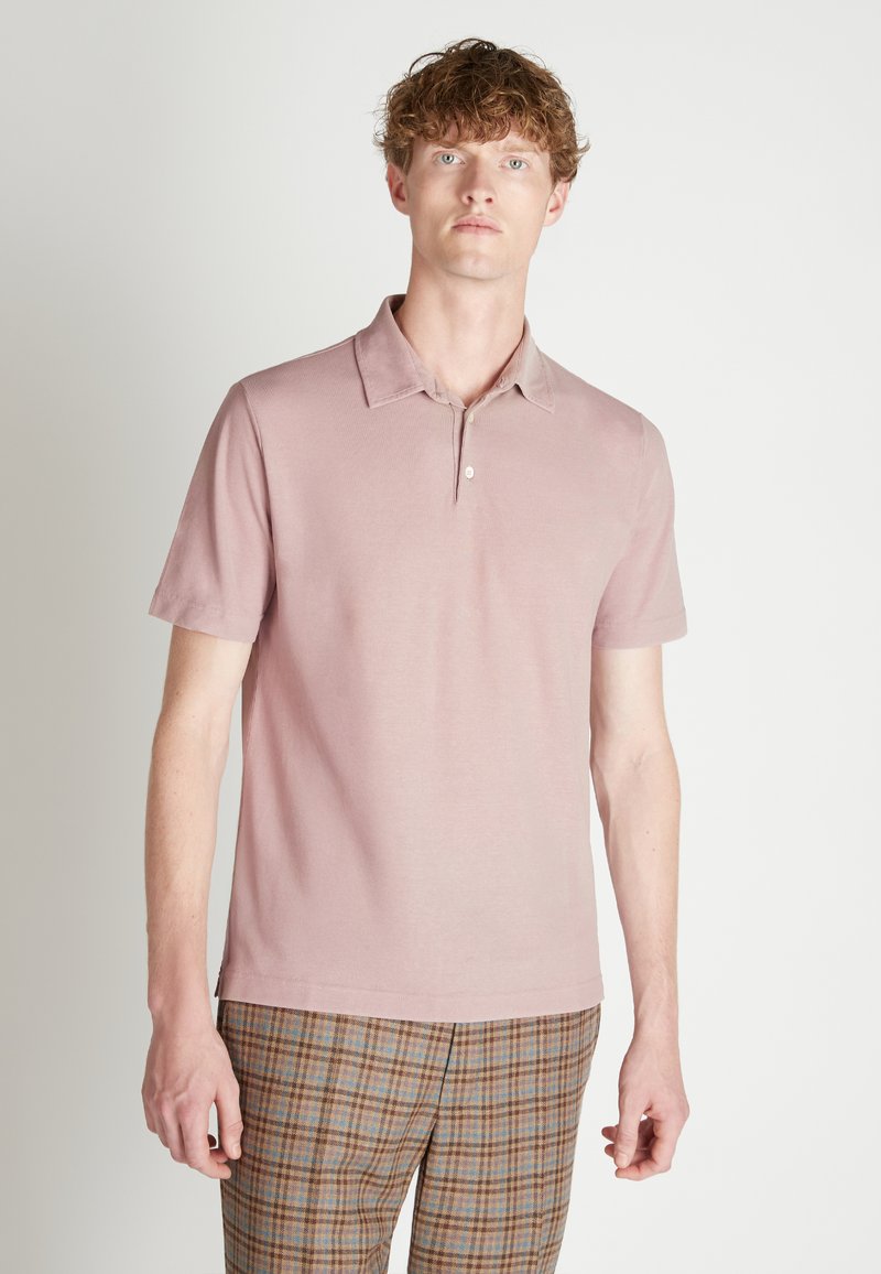 Roze polo shirt met korte mouwen en een kraag, met een enkele knop bij de nek en een gladde textuur. Draagt met een geruit broek.