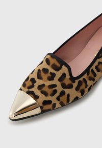 Sapatilha de padrão de leopardo com bico dourado metálico pontiagudo. Textura de pele suave com contorno preto ao longo da abertura e sola interior rosa.