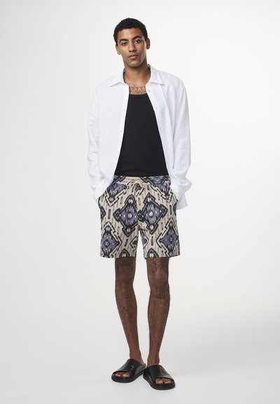 Herrklädsel med en vit linne skjorta med knappar, svart tanktop, mönstrade beige shorts med lila och svarta mönster, samt svarta sandaler.