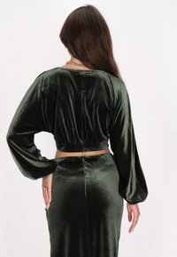Top cropped in velluto verde scuro con maniche lunghe e voluminose e vita arricciata. Tessuto liscio e design aderente che si abbina a una gonna coordinata.