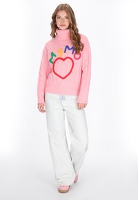 Pulover roz tricotat cu model, cu guler tip mock turtleneck, având text brodat colorat și o inimă. Asortat cu blugi deschiși și pantofi roz.