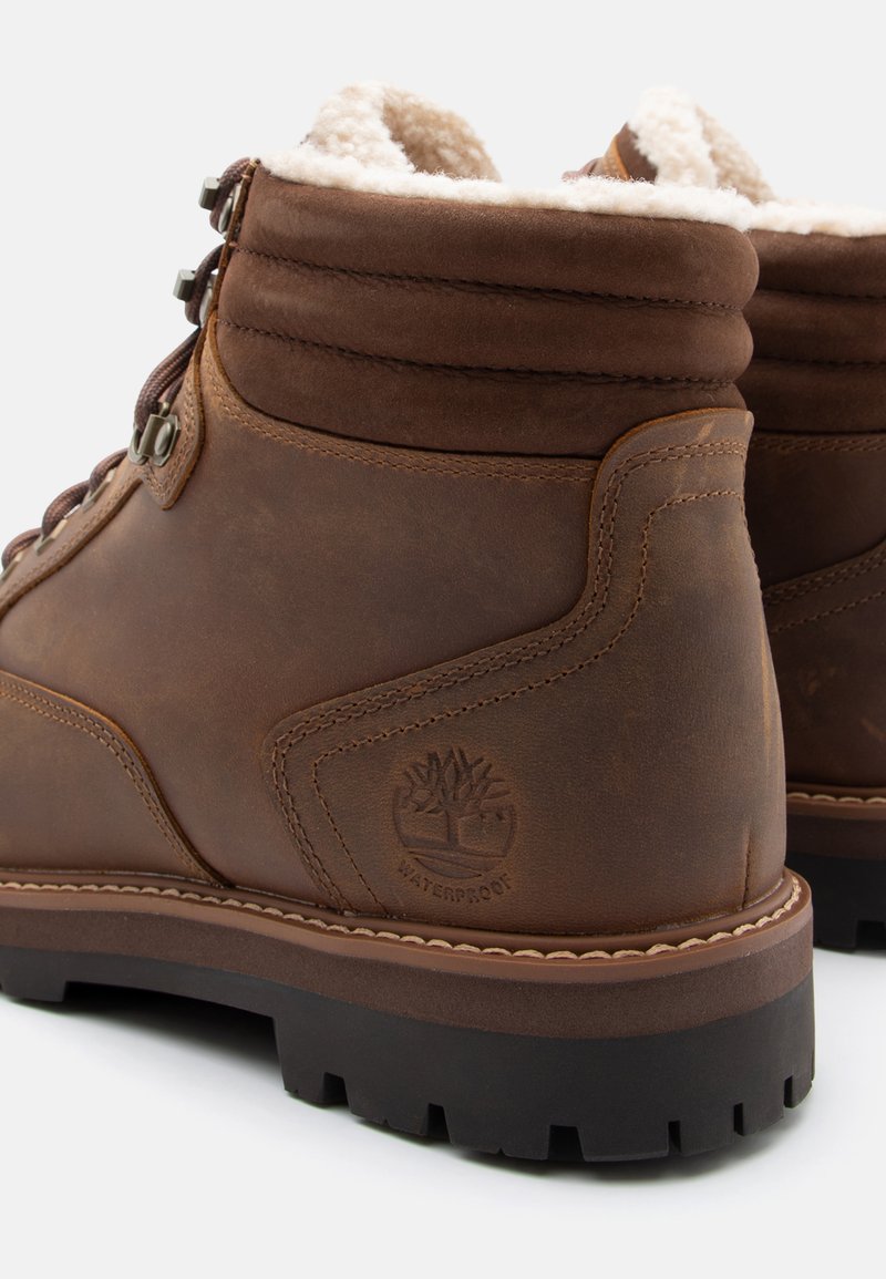 Braune, wasserdichte Wanderschuhe aus Leder mit gepolstertem Knöchelkragen, Metallösen und Fleece-Futter, fotografiert von hinten und von der Seite.