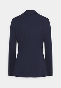 Marinblå blazer med en slät tygkvalitet, medfällda slag och långa ärmar. Har subtila sömmar och en figursydd siluett. Endast bakvy.