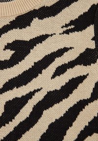 Beige gebreide stof met een zwart tijgerstreepjespatroon, met een gestructureerd oppervlak en een geribbelde halslijn.