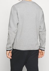 Felpa grigia con maniche lunghe e scollo rotondo. Presenta un tessuto strutturato e un bordo scuro a contrasto all'orlo.