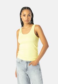 Kollane ribaga tank top laiate rihmadega, sobiv siluett ja pehme tekstuur, koos heledate kulunud denimitest teksapükstega.