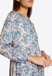 Vestido floral con un fondo rosa pastel y patrones de plantas azules y verdes. Manga larga con puños acampanados y un ajuste relajado.