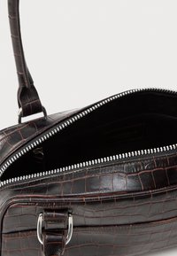 Fekete műbőr kézitáska krokodilbőr mintázattal, cipzárral és ezüst színű kiegészítőkkel. A belseje sötét, egyetlen rekesszel rendelkezik.