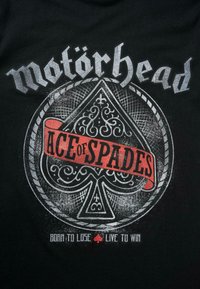 Melnā T-krekla, kuram ir balts un sarkans grafiskais dizains. Centrā esošs kāršu sirds simbols, ko apņem grezni raksti, ar tekstu "Motörhead" un "Ace of Spades".