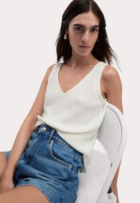 Vit, stickad linne med V-ringning och breda axelband, tillsammans med blå denimshorts med fransade nederkanter och framfickor.