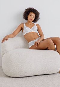 Witte kanten lingerie set met bloemmotieven, gecombineerd met een textuur, romige pluche bank. Glad huidtint smelt samen met de lichte achtergrond.