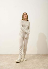 Světle šedý žebrovaný svetr s kulatým výstřihem, doplněný odpovídajícími jogger kalhotami. Bílá pozadí a neutrální boty dokončují vzhled.