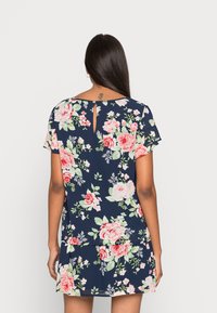 Vestido floral azul marinho com mangas curtas, apresentando padrões florais em rosa e verde, uma abertura em gota nas costas e uma silhueta fluida.
