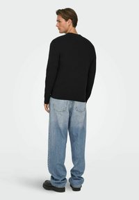 Maglietta nera a maniche lunghe con scollatura tonda, abbinata a jeans larghi celeste chiaro e scarpe nere con plateau. Vista da dietro.