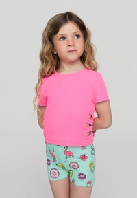 Top corto a maniche corte rosa a coste con ritagli laterali, abbinato a pantaloni corti verde menta con una stampa colorata di fenicotteri, ciambelle e fiori.